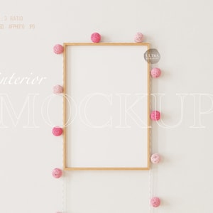 Puede incluir: Una maqueta de marco de madera con fondo blanco, rodeada de una cadena de bolas de lana rosa. El texto "interior mockup" está escrito en blanco en la pared.