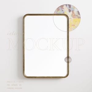 May include: A rectangular gold-framed mirror with rounded corners, set against a white background. The mirror's surface is blank, with the word "Mockup" in a light font. A circular detail in the upper right corner shows a colorful abstract design.
