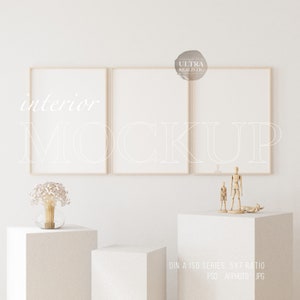May include: Three wooden frames with white mats and white backgrounds hang on a white wall.  The frames are arranged in a row, with the middle frame slightly higher than the other two.  Below the frames are two white cube pedestals, one taller than the other.  A small bouquet of dried flowers in a clear glass vase sits on the smaller pedestal.  Two wooden figurines stand on the larger pedestal.  The text "DIN A ISO SERIES. 5X7 RATIO. PSD. AFFPHOTO. JPG" is printed below the pedestals.