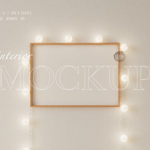 Puede incluir: Una maqueta de marco de madera con fondo blanco, colgada en una pared blanca con una cadena de luces blancas colgando a cada lado del marco. El texto "interior mockup" está escrito en blanco en la pared.