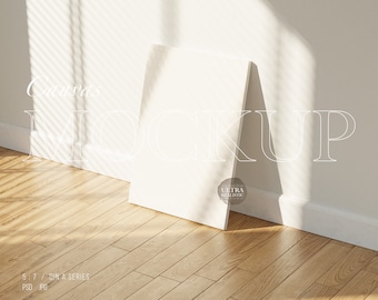 Könnte beinhalten: Ein weißer Leinwand-Mockup, der an einer weißen Wand mit Holzboden lehnt. Die Leinwand ist leer und bereit für Ihr Design. Der Text "Canvas Mockup" ist in Weiß an die Wand geschrieben.