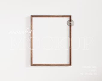 May include: A brown wood frame mockup on a white wall. The frame is empty and ready for your design.  "minimalist MOCKUP" is written in white text on the wall.