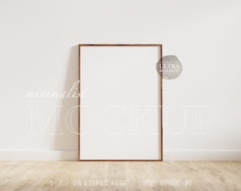 May include: A brown wooden frame mockup with a white background. The frame is on a light wood floor and a white wall. The text "minimalist MOCKUP" is written in white on the wall. The text "ULTRA REALISTIC" is written in white on a brown watercolor circle. The text "5:7 / DIN A SERIES RATIO PSD AFPHOTO JPG CHANGEABLE WALL" is written in white on the floor.