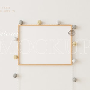 Puede incluir: Una maqueta de marco de madera con fondo blanco. El marco está colgado en una pared blanca con una cadena de pompones blancos y amarillos que cuelgan de la parte superior del marco. El texto "interior mockup" está escrito en blanco en la pared.
