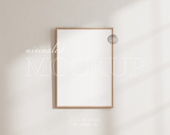 May include: A minimalist mockup featuring a light wood frame with a white background. The frame is hanging on a white wall with a subtle shadow. The text "minimalist MOCKUP" is written in white on the wall.