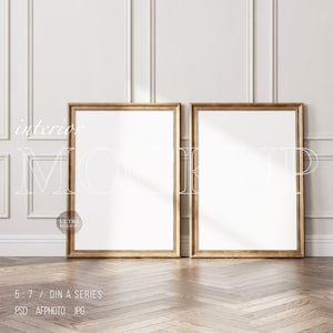 Könnte beinhalten: Zwei goldene Bilderrahmen mit weißen Passepartouts sind an einer weißen Wand mit dekorativen Leisten angebracht. Die Rahmen sind leer und bereit für Ihre Kunstwerke oder Fotos.