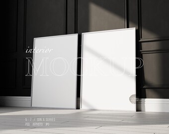 May include: Two white framed posters leaning against a black wall with white trim. The posters are blank and ready for your design.