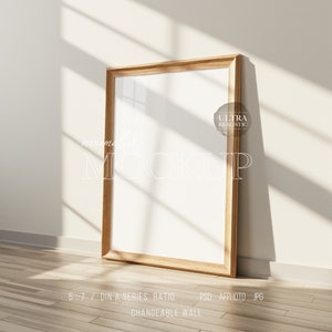 May include: A wooden frame mockup with a white background, standing on a wooden floor. The frame is in a room with a white wall and sunlight streaming through a window. The text "minimalist MOCKUP" is written in white on the wall. The text "ULTRA REALISTIC" is written in white on a circle with a black outline. The text "5:7 / DIN A SERIES RATIO PSD AFPHOTO JPG CHANGEABLE WALL" is written in black on the floor.