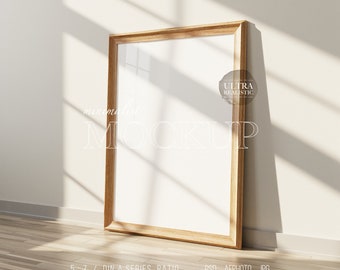 May include: A wooden frame mockup with a white background, standing on a wooden floor. The frame is in a room with a white wall and sunlight streaming through a window. The text "minimalist MOCKUP" is written in white on the wall. The text "ULTRA REALISTIC" is written in white on a circle with a black outline. The text "5:7 / DIN A SERIES RATIO PSD AFPHOTO JPG CHANGEABLE WALL" is written in black on the floor.