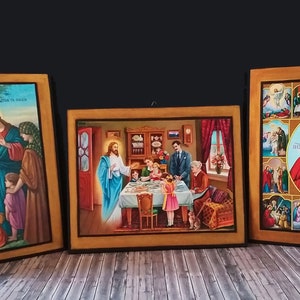 May include: Three framed religious paintings depicting scenes from the life of Jesus Christ. The paintings are on a wooden background and feature a gold frame. The first painting shows Jesus teaching children. The second painting shows Jesus at a table with people. The third painting shows Jesus in the centre of a grid of nine smaller paintings, each depicting a different scene from the life of Jesus.