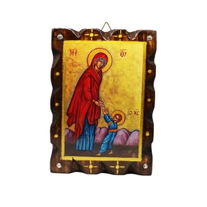 May include: A wooden icon depicting the Virgin Mary and baby Jesus. The icon is painted in a traditional style with bright colours. The Virgin Mary is wearing a red robe and blue dress, and she is holding baby Jesus in her arms. The icon is framed in a dark wood frame with a gold trim.