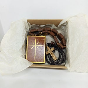 Op de afbeelding: Een houten doos met een bruin deksel met daarin een houten kruis ketting en een houten hanger met een gouden kruis ontwerp.