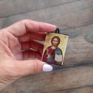 May include: A small wooden icon of Jesus Christ with a black frame and a gold background. The icon depicts Jesus with a red robe and a blue cloak, holding a book in his left hand and making a blessing gesture with his right hand. The text "XC" is visible in the top right corner of the icon.
