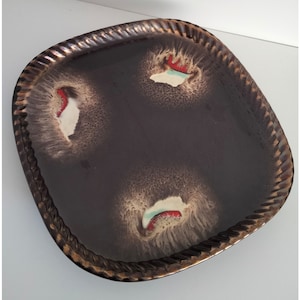 Op de afbeelding: Een bruin keramiek bord met een decoratief ontwerp met witte, rode en groene swirls. Het bord heeft een verhoogde rand en een textuur.