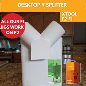 May include: A white desktop Y splitter with the text "DESKTOP Y SPLITTER". The image also includes the text "ALL OUR F1 JIGS WORK ON F2" and "XTOOL F2 F1". The image also shows two laser engravers.