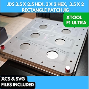 Op de afbeelding: Een close-up van een grijze rechthoekige patch jig met meerdere zeshoekige en rechthoekige uitsparingen. De jig is gelabeld "XTOOL F1 ULTRA" en "JDS 3.5 X 2.5 HEX, 3 X 2 HEX, 3.5 X 2 RECTANGLE PATCH JIG". De tekst "XCS & SVG FILES INCLUDED" is ook zichtbaar.