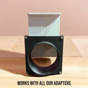 Peut inclure: Un adaptateur imprimé en 3D noir et gris pour un système de ventilation. L'adaptateur a une ouverture ronde et un cadre carré. Le texte "WORKS WITH ALL OUR ADAPTERS" est imprimé sous l'adaptateur.