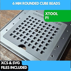 Puede incluir: Una bandeja de plástico gris con una cuadrícula de ranuras para cuentas cúbicas redondeadas de 6 mm. La bandeja está etiquetada como "XTOOL F1" y tiene una cuenta negra en una de las ranuras. El texto "XCS & SVG FILES INCLUDED" está en la parte inferior de la imagen.