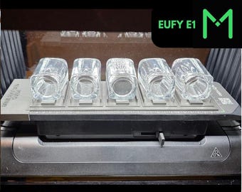 Könnte beinhalten: Eine Shotglashalterung mit fünf durchsichtigen, quadratischen Shotgläsern. Der Text "SHOT GLASS JIG" und "FOR UV PRINTERS" sind grün. Der Text "EUFY E1" ist schwarz mit einem grünen "M"-Logo.