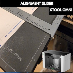 Puede incluir: Una guía de alineación gris impresa en 3D para la máquina láser xTool Omni. La herramienta cuenta con una regla integrada con marcas en pulgadas, el texto OMNI ALIGNMENT SLIDER y una guía de colocación de papel con el texto Maximum y Feed one sheet at a time.