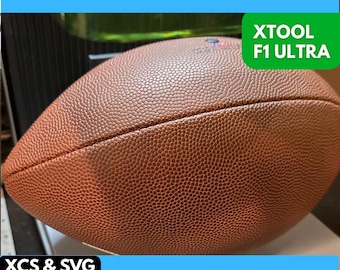 Può includere: Un pallone da football americano in pelle marrone con cuciture bianche. Il pallone è su una superficie blu con il testo "XTOOL F1 ULTRA" in verde e "XCS & SVG FILES INCLUDED" in nero.