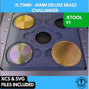 May include: A blue plastic tray with five circular cutouts for holding round metal blanks. The tray has the text "EBP-84" printed on it. Two of the cutouts are filled with gold-colored metal blanks, one is filled with a silver-colored metal blank, and two are empty. The tray is labeled "31.75MM - 40MM DELUXE BRASS CHALLANGER" and "XTOOL F1".