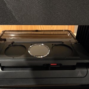 May include: A black 3D printer with the text "MAKE E1 A" and "CREATIVE 3D Eng" in white. The printer has a tray with three circular openings and a red indicator light.