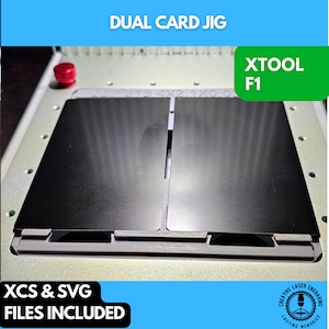 May include: A metal dual card jig with two black cards in place. The text "DUAL CARD JIG" is at the top, and "XTOOL F1" is in a green box. The bottom text reads "XCS & SVG FILES INCLUDED".