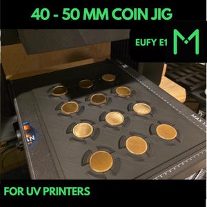 May include: A black coin jig with multiple circular slots holding gold-colored coins. The text "40 - 50 MM COIN JIG" and "FOR UV PRINTERS" are displayed in green. The jig is designed for coins approximately 1.57 to 1.97 inches in diameter.
