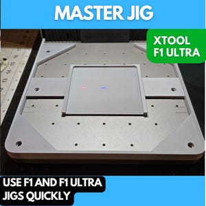 May include: A white plastic jig with the text "MASTER JIG" and "XTOOL F1 ULTRA" printed on it. The jig has a square cutout in the center and multiple small holes around the edges. The text "USE F1 AND F1 ULTRA JIGS QUICKLY" is printed below the jig.