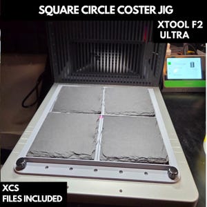 May include: A laser engraving machine with the text "SQUARE CIRCLE COSTER JIG" and "XTOOL F2 ULTRA". The machine holds four gray square coasters. The text "XCS FILES INCLUDED" is also visible.