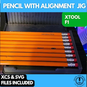 May include: A gray 3D printed jig for aligning pencils. The jig has a slot for holding multiple pencils. The pencils are yellow with black writing that says "I AM BEAUTIFUL" and "Madisi #2 HB". The jig is labeled "XTOOL F1" and "XCS & SVG FILES INCLUDED".