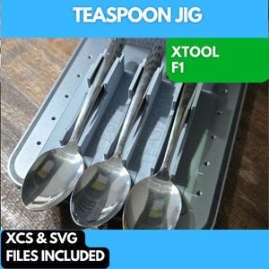 Könnte beinhalten: Ein grauer 3D-gedruckter Jig zum Halten von Teelöffeln, beschriftet "XTOOL F1 Teaspoon Jig". Der Jig ist so konzipiert, dass er drei Teelöffel in vertikaler Position hält. Der Jig befindet sich auf einer grauen Oberfläche. XCS- und SVG-Dateien sind enthalten.