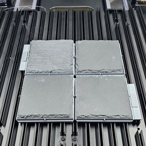 May include: Four square black slate tiles with gray frames, arranged in a 2x2 grid on a black metal surface.