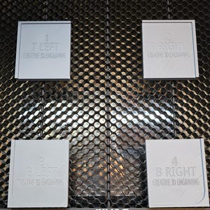 May include: Four gray square plaques with rounded corners, each with a number and text. The plaques are labeled "1 T LEFT CREATIVE 3D ENGRAVING", "2 T RIGHT CREATIVE 3D ENGRAVING", "3 B LEFT CREATIVE 3D ENGRAVING", and "4 B RIGHT CREATIVE 3D ENGRAVING". The plaques are arranged in a grid pattern on a black metal surface.