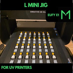 May include: A black L Mini Jig for UV printers, with rows of small, gray and white figures with yellow heads. The text "L MINI JIG", "CREATIVE 3D En", "EUFY E1", and "FOR UV PRINTERS" are visible in green.