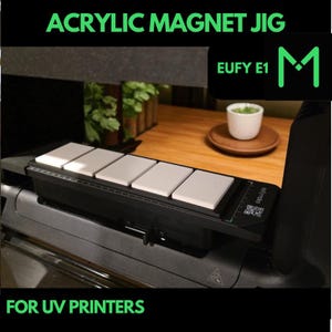 May include: Black acrylic magnet jig for UV printers. The jig has five white rectangular blocks and the text "ACRYLIC MAGNET JIG" and "FOR UV PRINTERS" in green. The product also has the text "EUFY E1" and a green "M" logo.