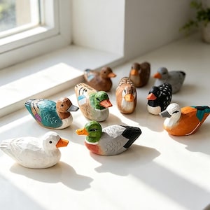 Pode incluir: Uma coleção de nove pequenas figuras de patos esculpidas à mão em madeira, cada uma com padrões e cores pintadas distintos, incluindo branco, verde, castanho, preto e laranja, exibidas juntas com texturas esculpidas visíveis.