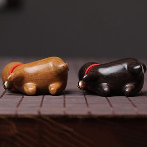 Peut inclure: Deux figurines d'animaux en bois, l'une brune et l'autre noire, avec des colliers rouges et de petites cloches. Les figurines sont couch&eacute;es sur le dos, les pattes en l'air.