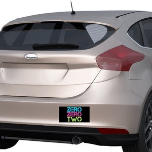 May include: A silver car with a black bumper sticker that says "ZERO ZERO TWO" in colorful letters.