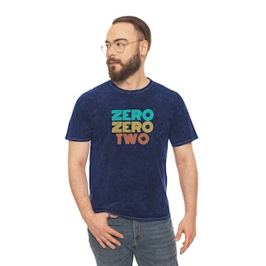 May include: A dark blue t-shirt with a vintage-style graphic that reads "ZERO ZERO TWO" in yellow, orange, and turquoise.