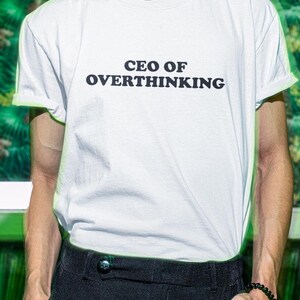 May include: White t-shirt with black text that reads "CEO OF OVERTHINKING".