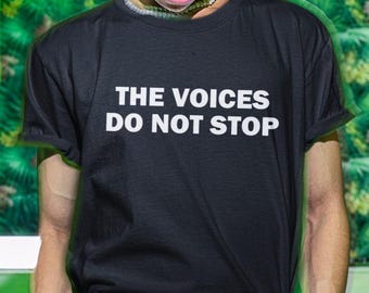 Könnte beinhalten: Schwarzes T-Shirt mit dem weißen Text "THE VOICES DO NOT STOP". Das Shirt hat kurze Ärmel und einen Rundhalsausschnitt. Der Hintergrund zeigt ein grünes und gelbes tropisches Muster.