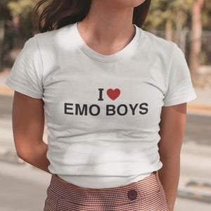 Może przedstawiać: Biała koszulka z nadrukiem "I ♥ Emo Boys" z przodu.