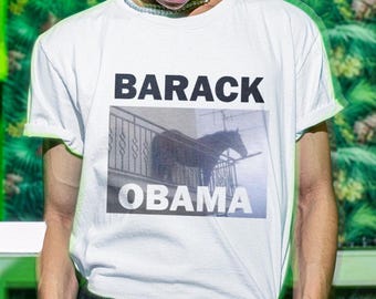 Pode incluir: Camiseta branca com uma foto em preto e branco de um cavalo em uma varanda. O texto "BARACK OBAMA" está impresso na camiseta.