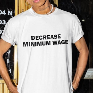 Puede incluir: Camiseta blanca con el texto "DECREASE MINIMUM WAGE" impreso en negro.