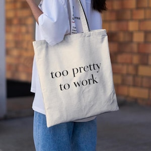 Puede incluir: Una bolsa de lona blanca con texto negro que dice "too pretty to work".