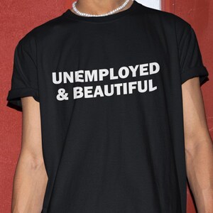 May include: Black t-shirt with white text that reads "UNEMPLOYED & BEAUTIFUL".
