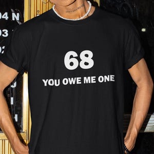 May include: Black t-shirt with white text that says "68 You Owe Me One"