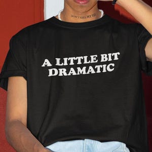 May include: Black t-shirt with white text that reads "A little bit dramatic".